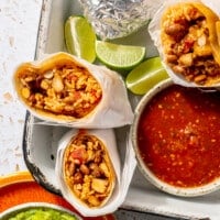 Halved chicken burritos on a tray next to salsa and guacamole.