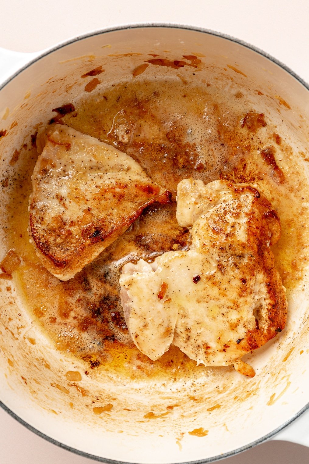 Two chicken breasts searing in a large enameled cast iron pot.