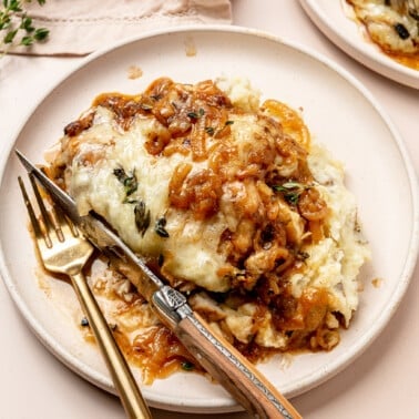 A french onion chicken breast smothered in gruyere cheese and caramelized onions next to mashed potatoes.