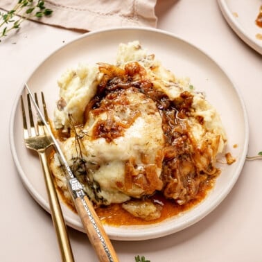 A french onion chicken breast smothered in gruyere cheese and caramelized onions next to mashed potatoes.