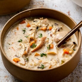 A bowl of creamy chicken and wild rice soup with a bronze spoon sticking out of it.