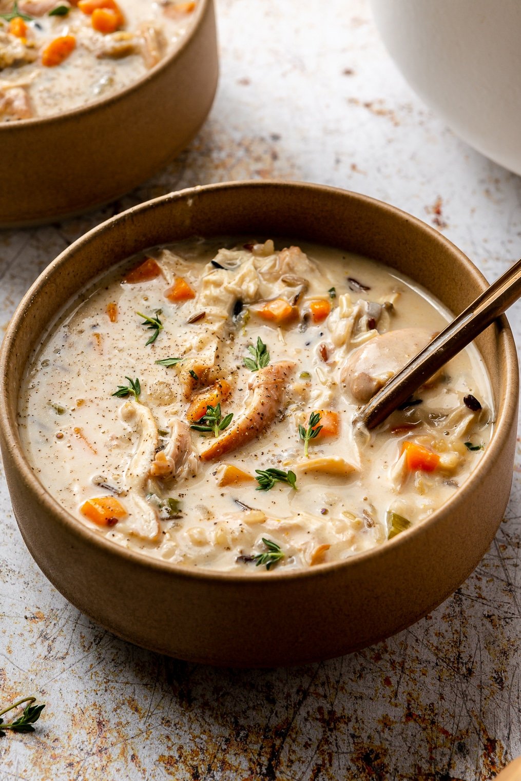 A bowl of creamy chicken and wild rice soup with a bronze spoon sticking out of it.