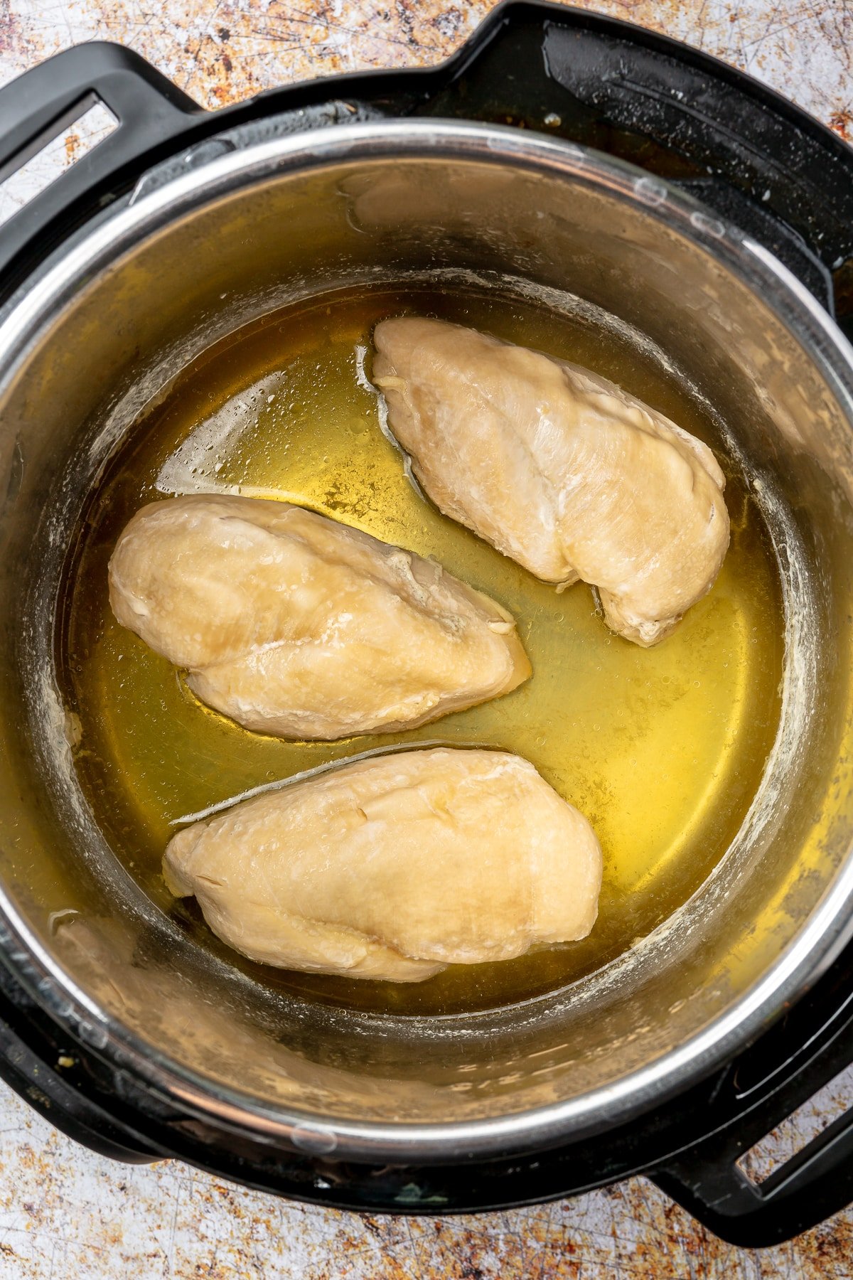 Three chicken breasts sit, surrounded by oil, in a pressure cooker.