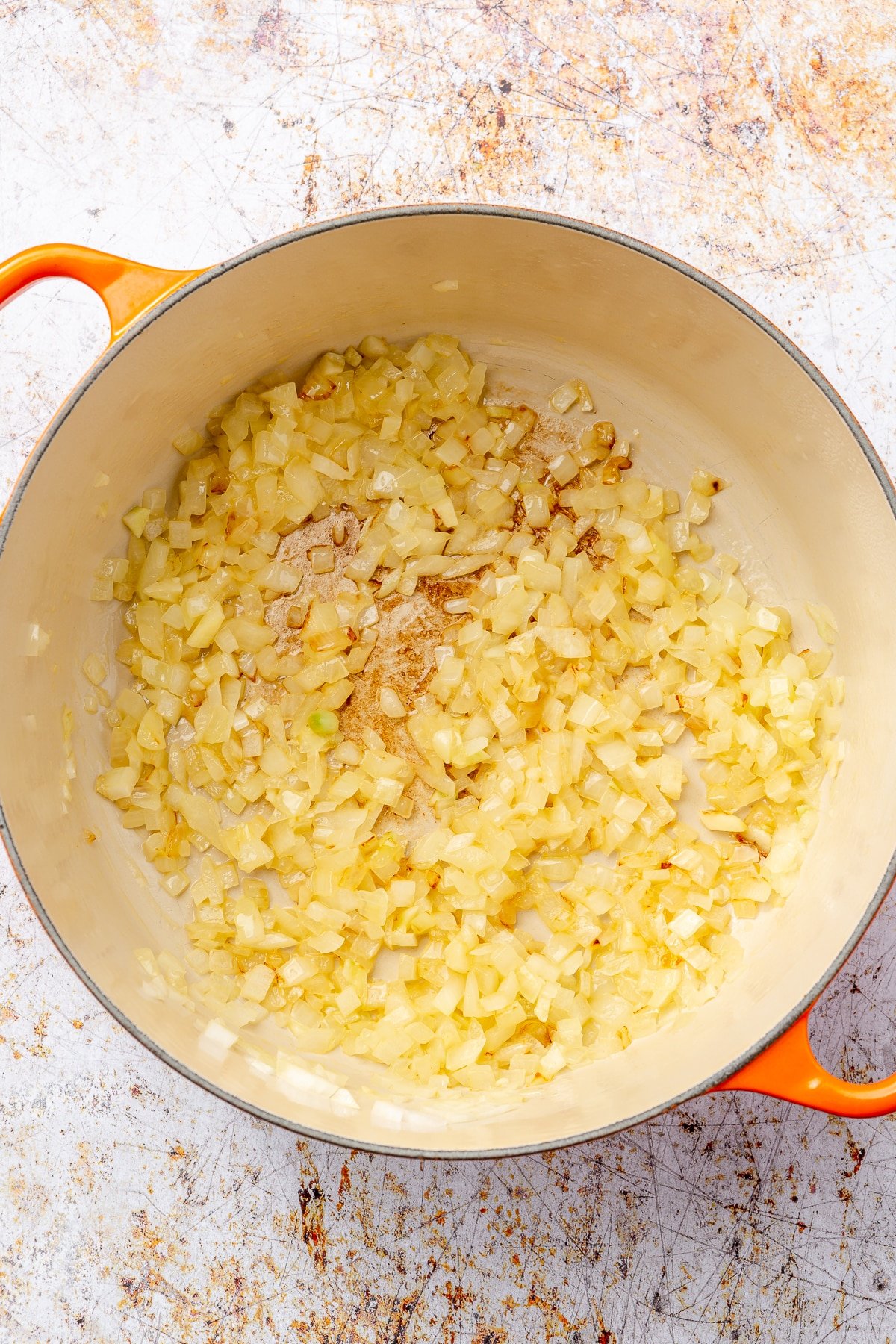 Slightly browned and translucent chopped onions sit in an enameled pot.