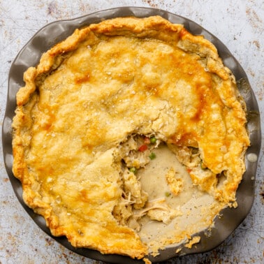 The top view of a fully cooked chicken pot pie is shown still in its baking dish. A slice has been removed and bits of filling spill into the open space.