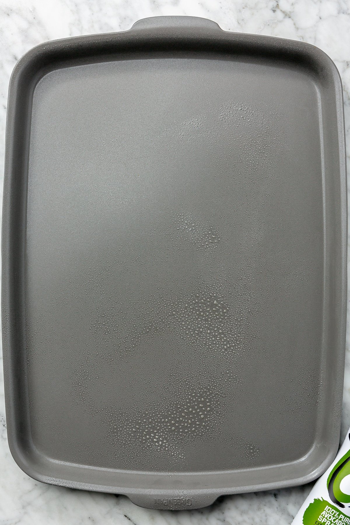 A nonstick baking pan has been greased and sits on a marble countertop.