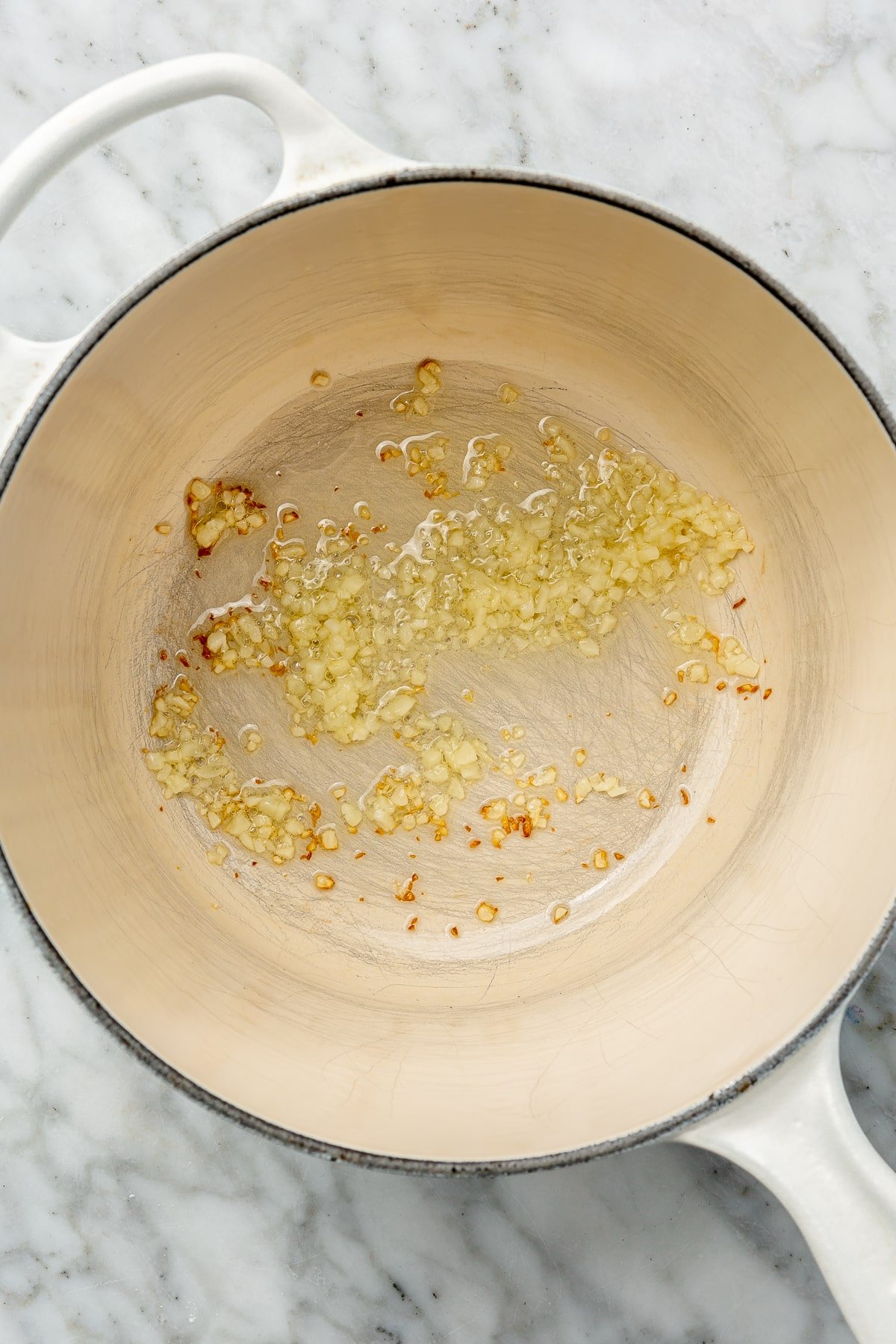 Minced garlic, oil, and variety of spices have been added to a nonstick, stovetop pan.