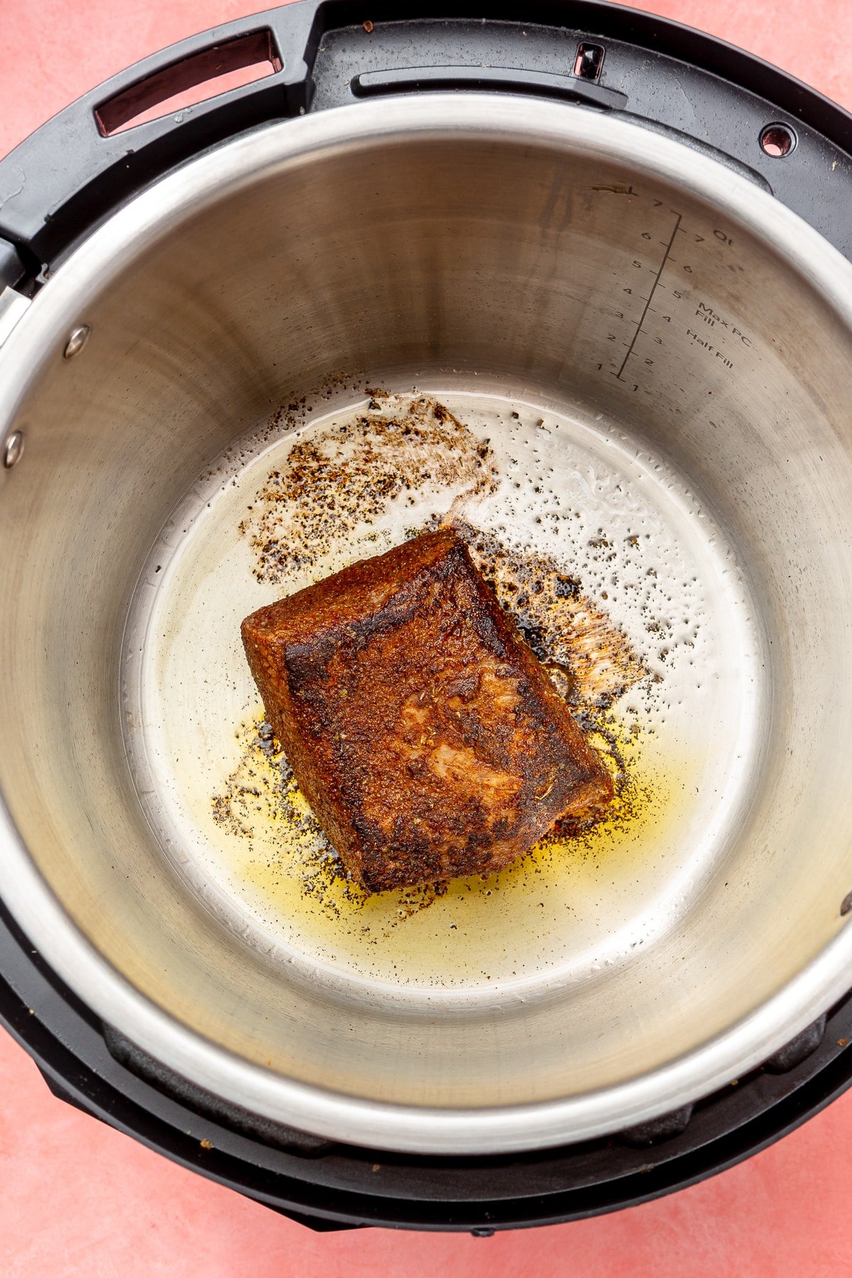 A rectangular piece of beef brisket is being seared in an instant pot. It is golden brown in color.