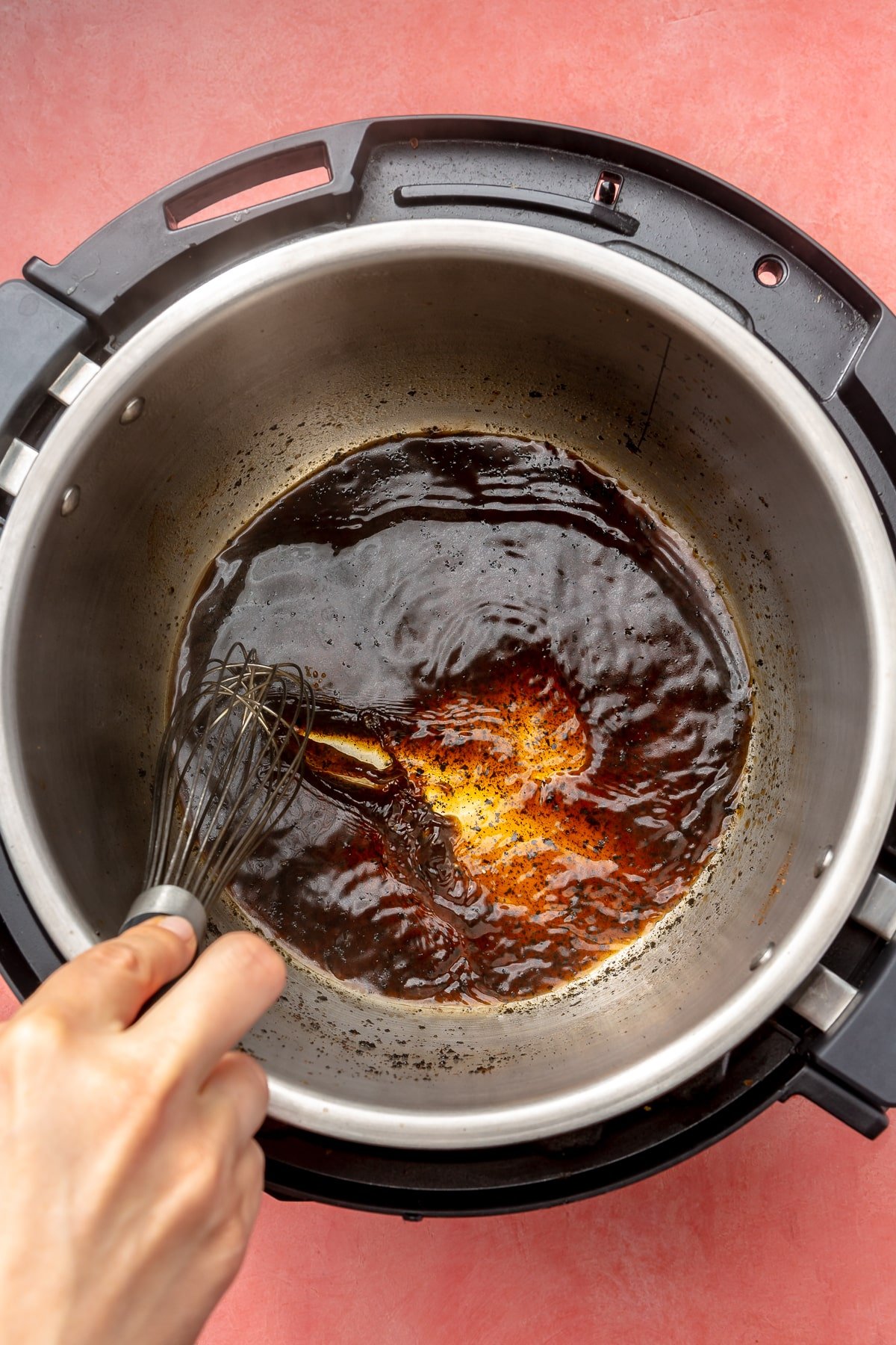 A hand is shown, using a whisk, mixing a thick brown sauce which sits in the bottom of an instant pot.