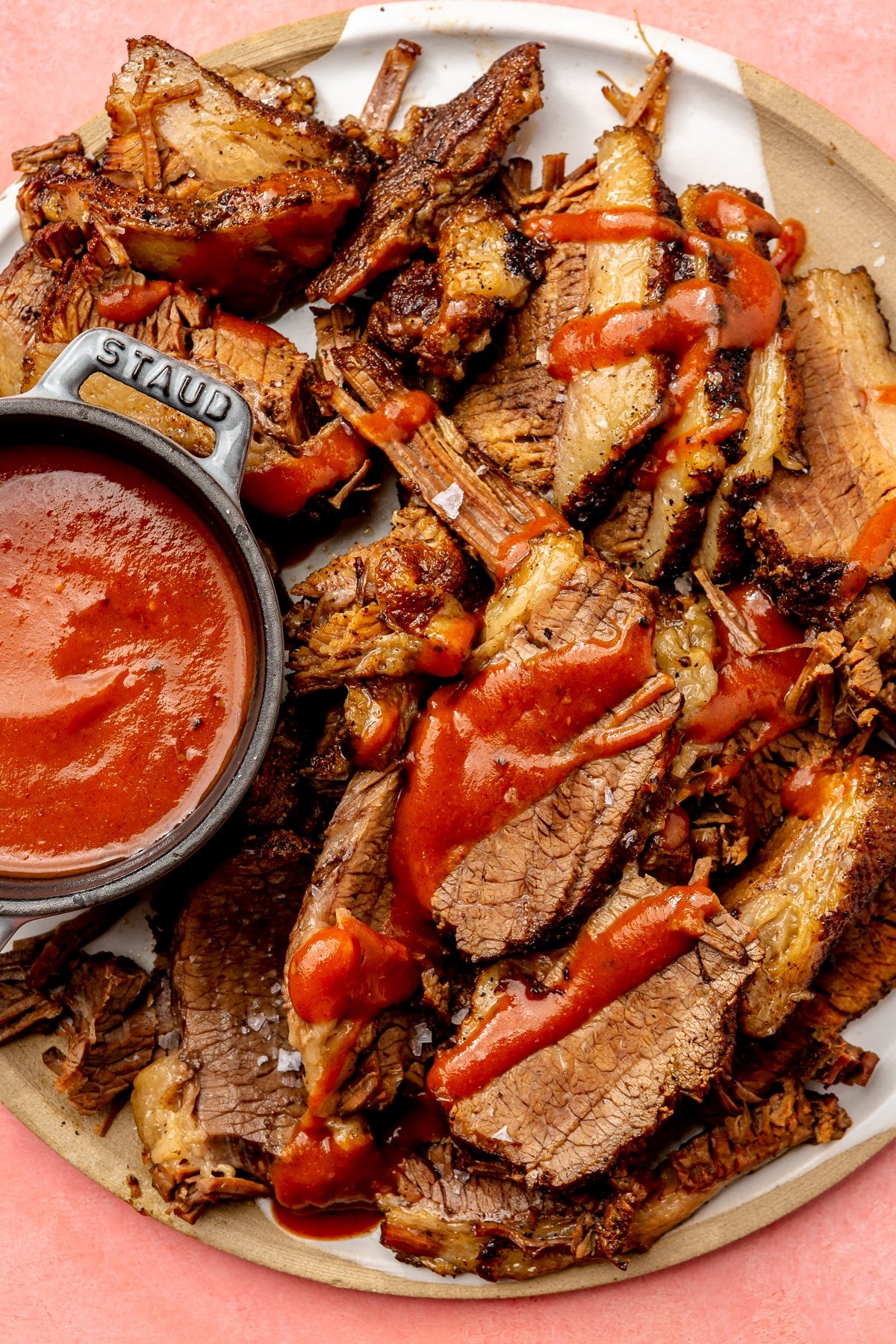 Sliced beef brisket sits on a brown plate. It has been drizzled with a red barbecue sauce. A bowl of sauce sits on the side.