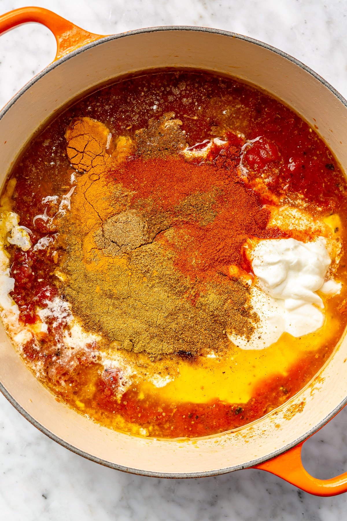 Canned tomatoes, yogurt, and spices in a large enameled cast iron pot.