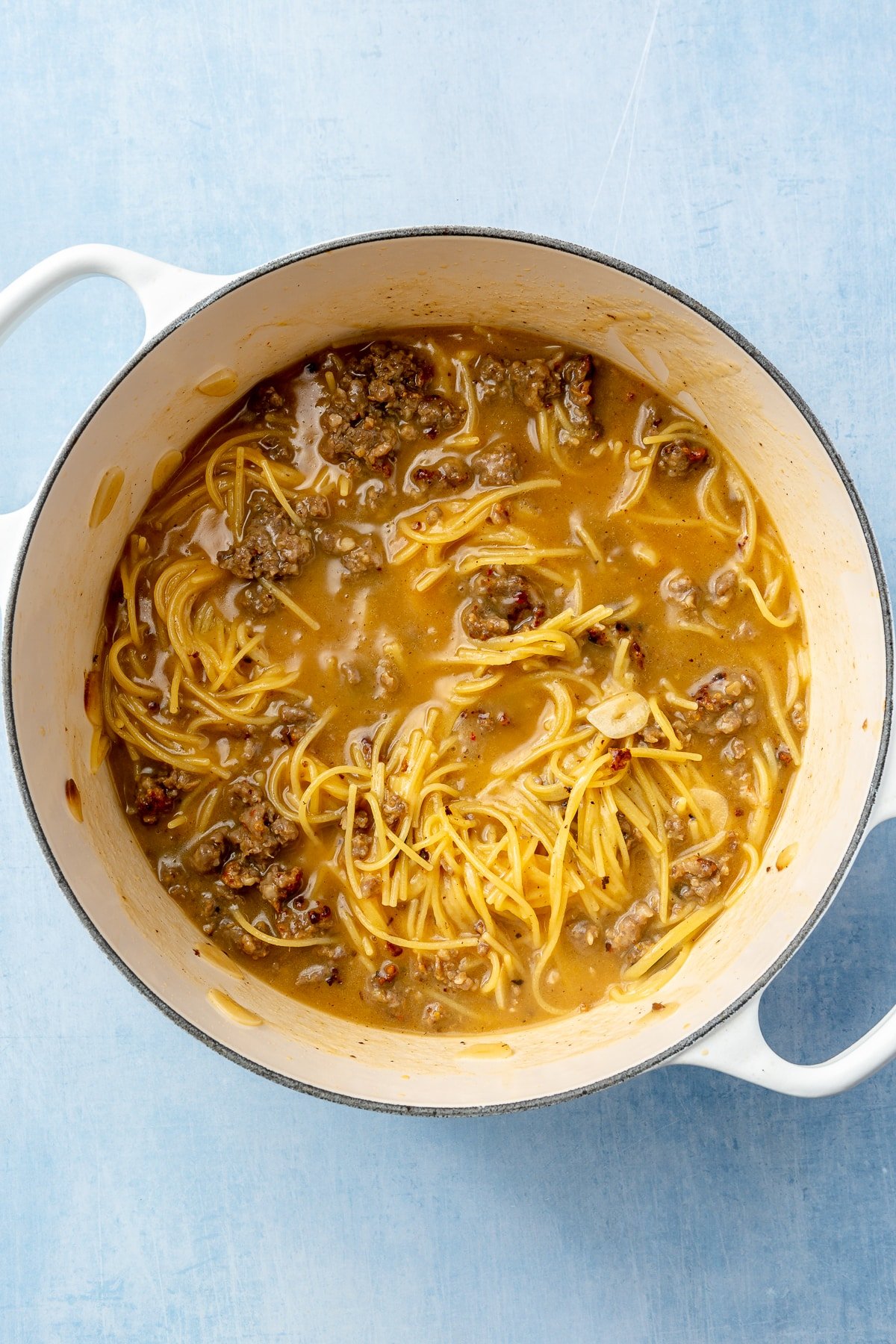 Thee spaghetti, sauce, and sausage have been fully cooked and stirred in a white, enameled pot.