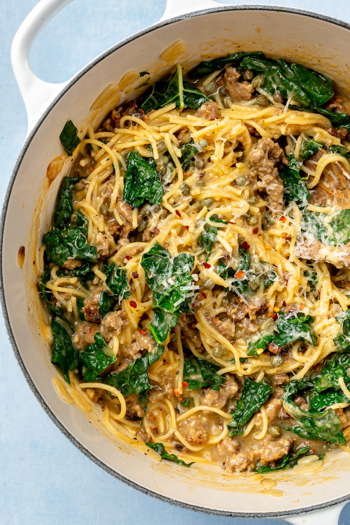 Parmesan cheese has been stirred into the kale, sausage, and spaghetti mixture. Red pepper flakes have been added to the top.