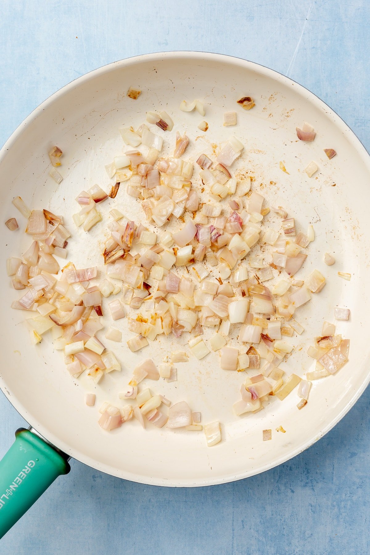 Onions are being lightly browned in a frying pan with a teal handle.