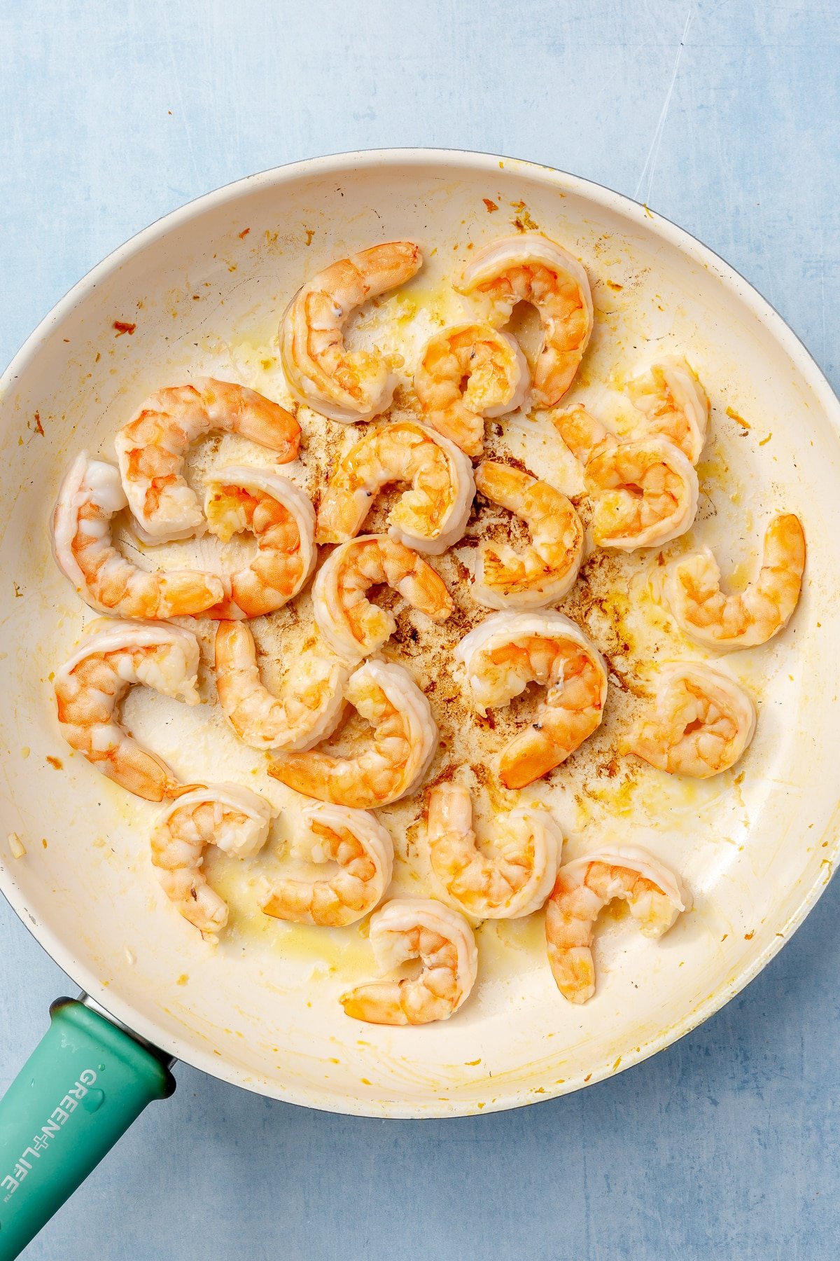 Cooked, lightly golden shrimp, sits in a frying pan with a teal handle.