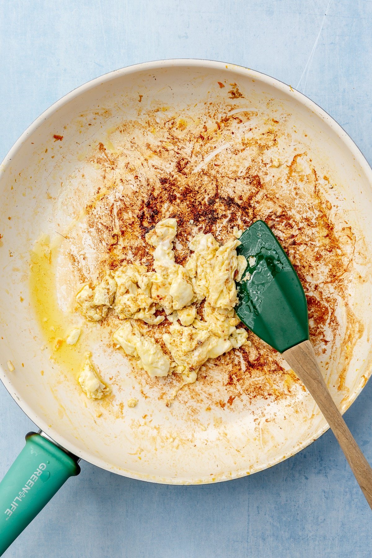 Egg has been scrambled in a frying pan with a teal handle. A green spatula sits on the side.