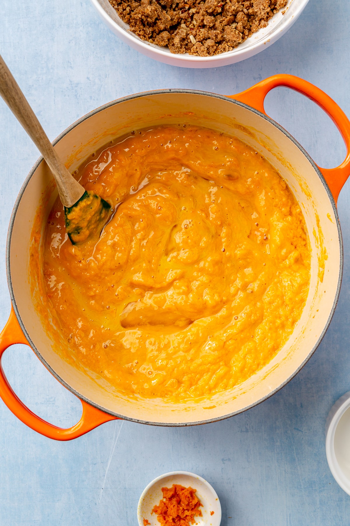 Sweet potato and the ingredients have been fully combined into a thick paste with a green spatula. The mixture sits in an orange, enameled pot.