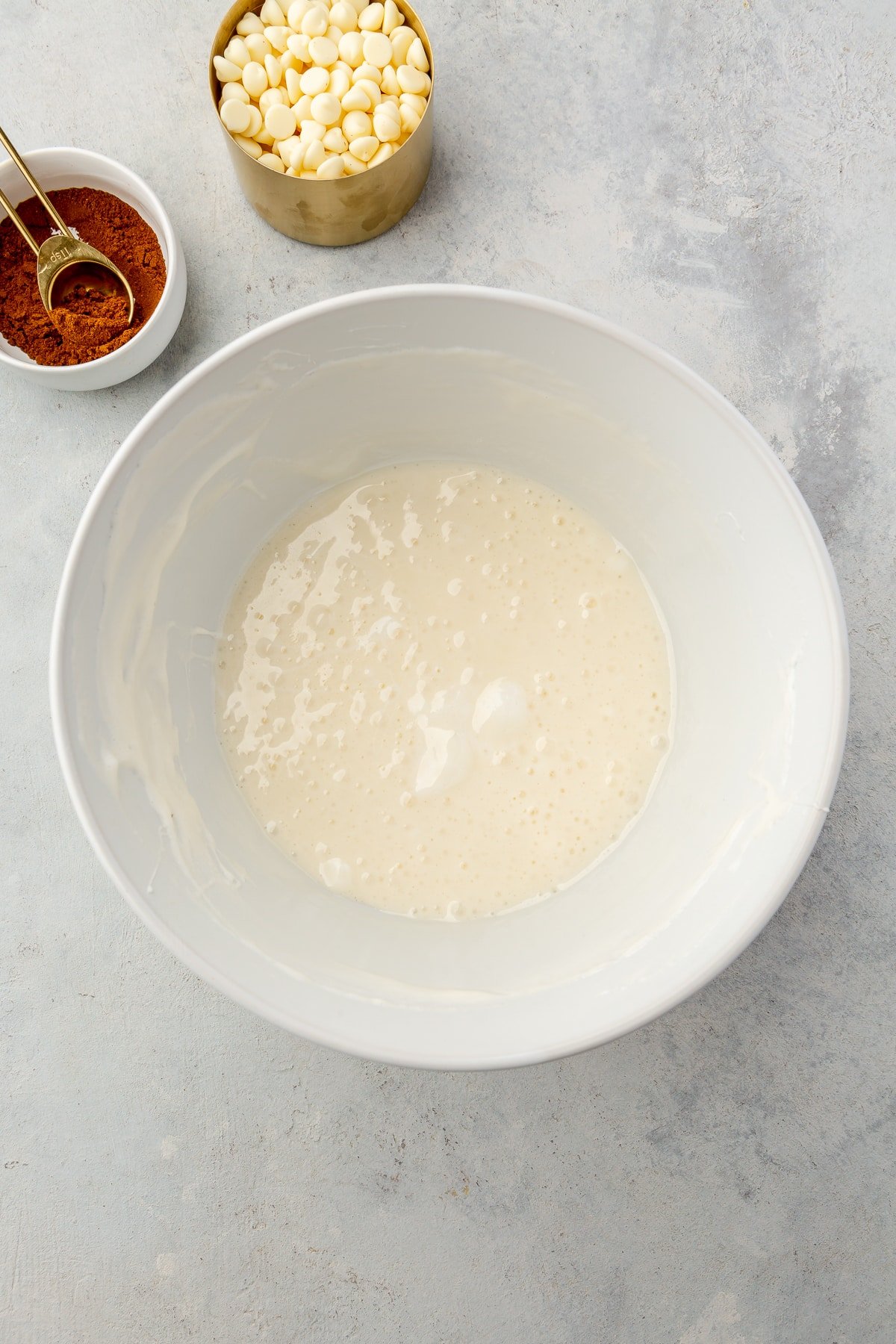 Melted butter and marshmallows in a large bowl next to white chocolate chips and pumpkin spice.