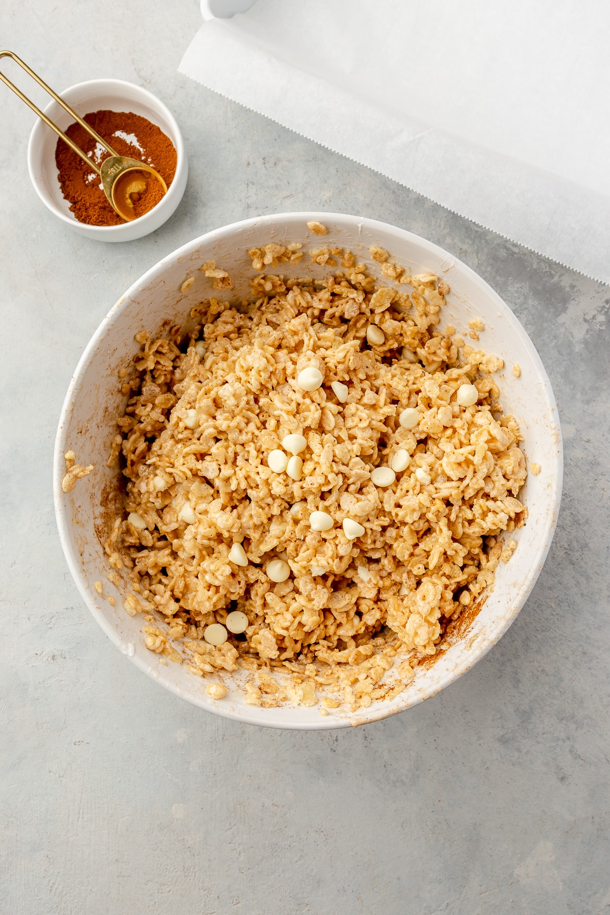 A rice krispie treat mixture (melted marshmallows, rice crisp cereal, white chocolate chips, and pumpkin spice) stirred together in a large bowl.