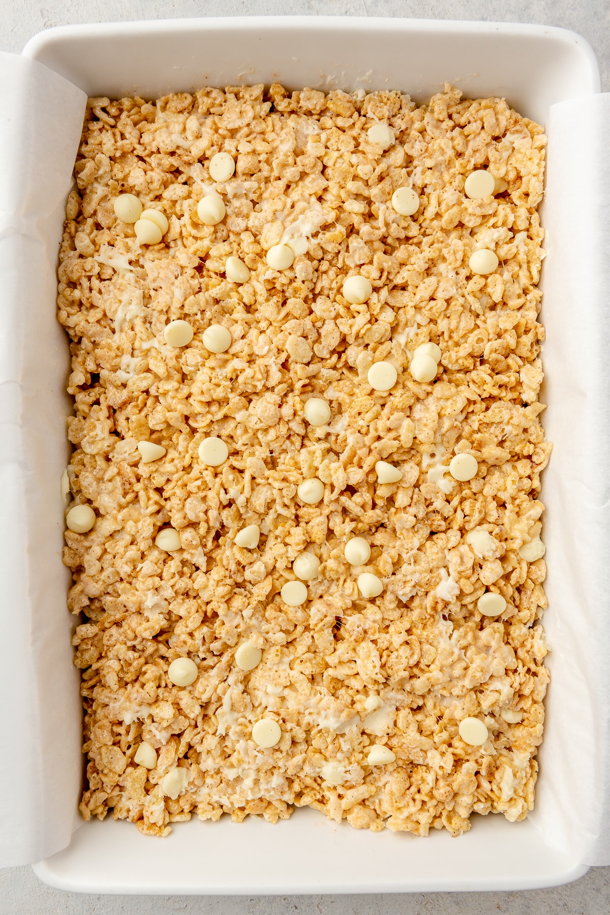 A pumpkin spice rice krispie treat mixture pressed into a parchment paper lined baking dish.