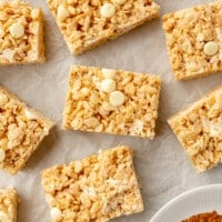 Sliced pumpkin spice rice krispie treats on parchment paper next to a small bowl of pumpkin pie spice.