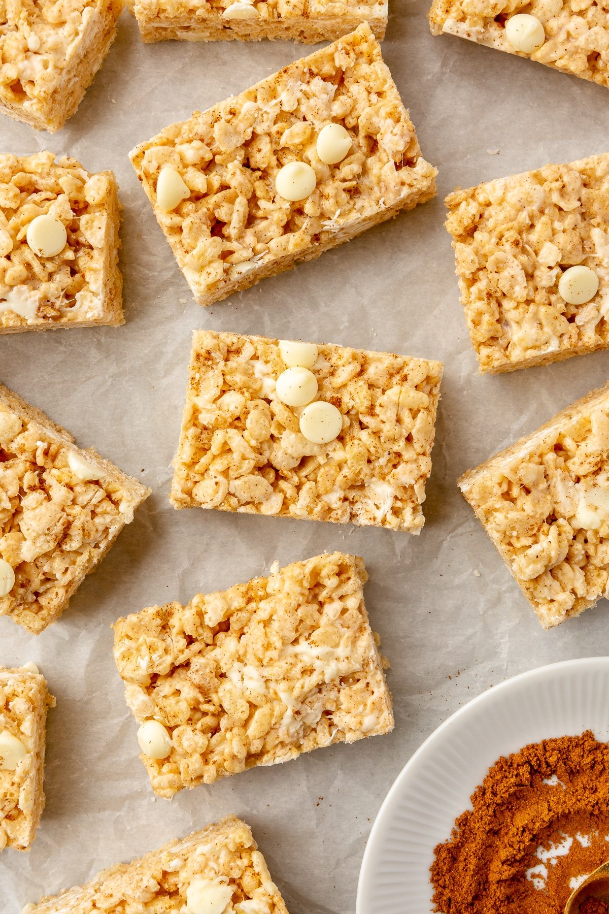 Sliced pumpkin spice rice krispie treats on parchment paper next to a small bowl of pumpkin pie spice.