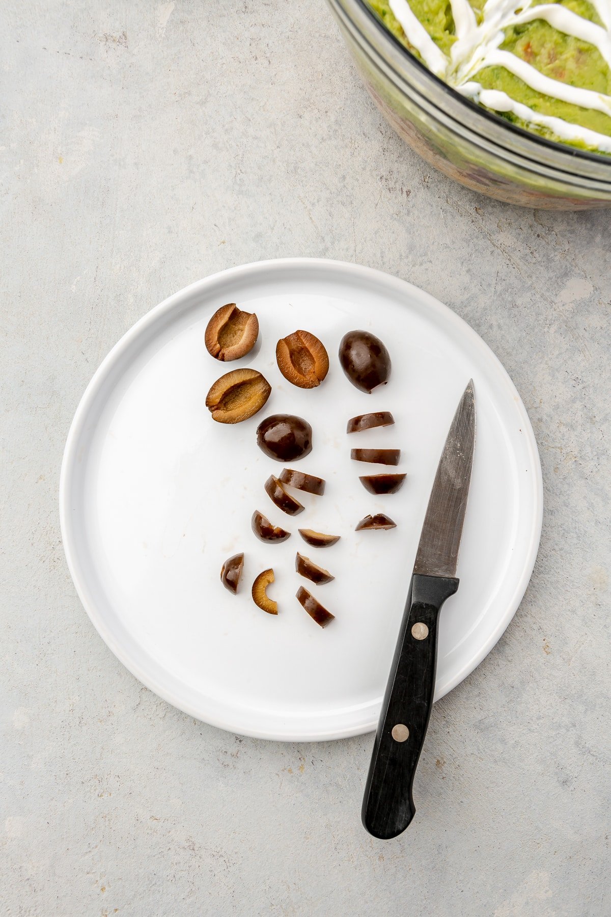 Black olives being sliced on a white plate.