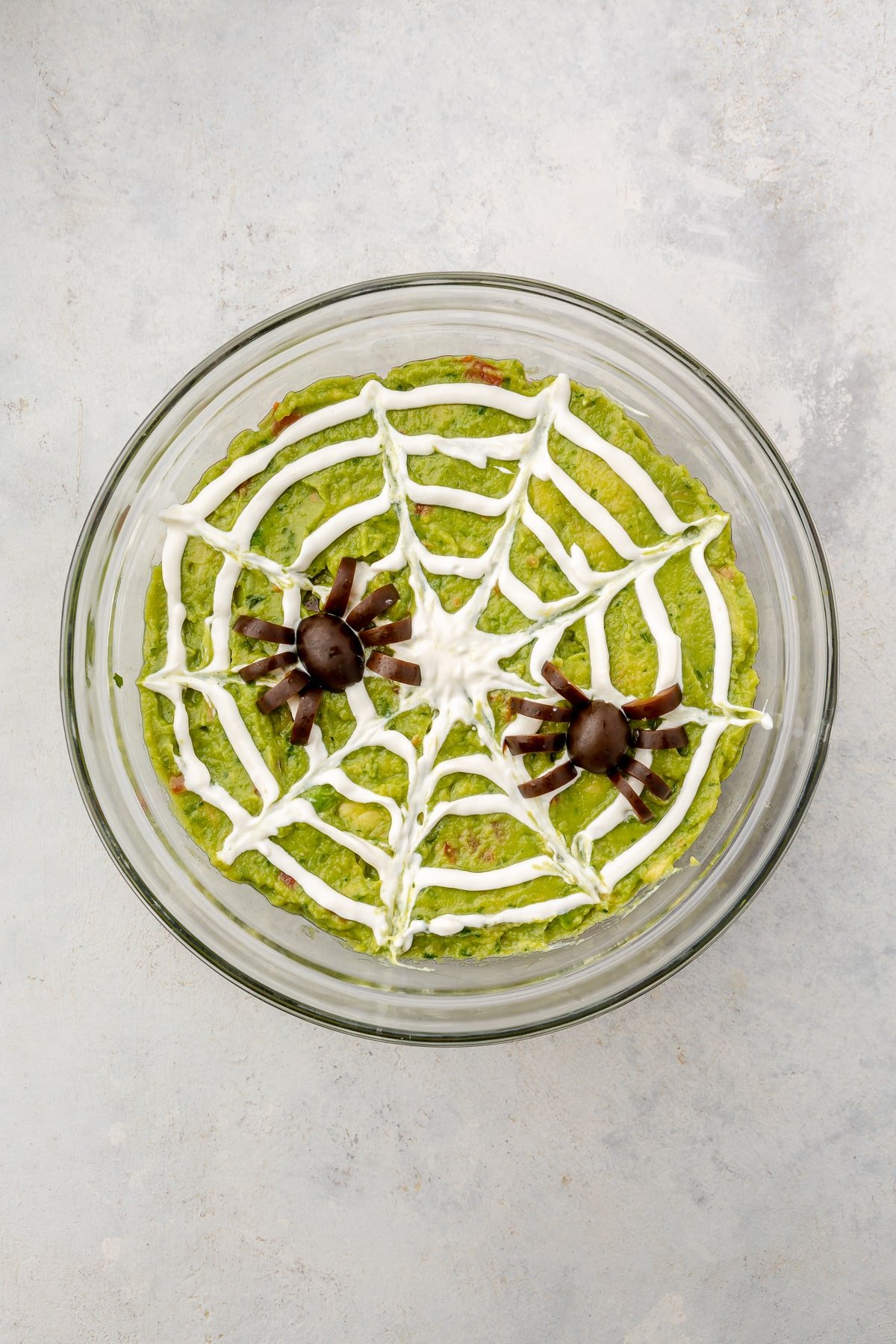 A finished bowl of spooky 7 layer dip complete with a sour cream spider web and black olive spiders on top.
