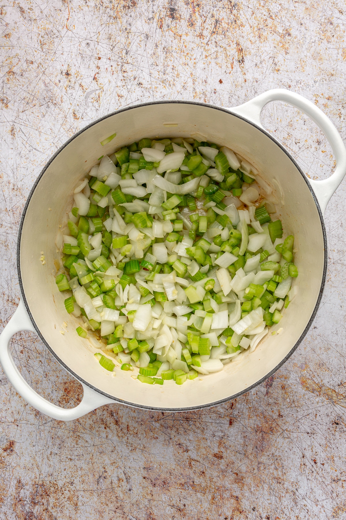 Chopped onion and celery has been added on top of th bacon in the white enameled pot.