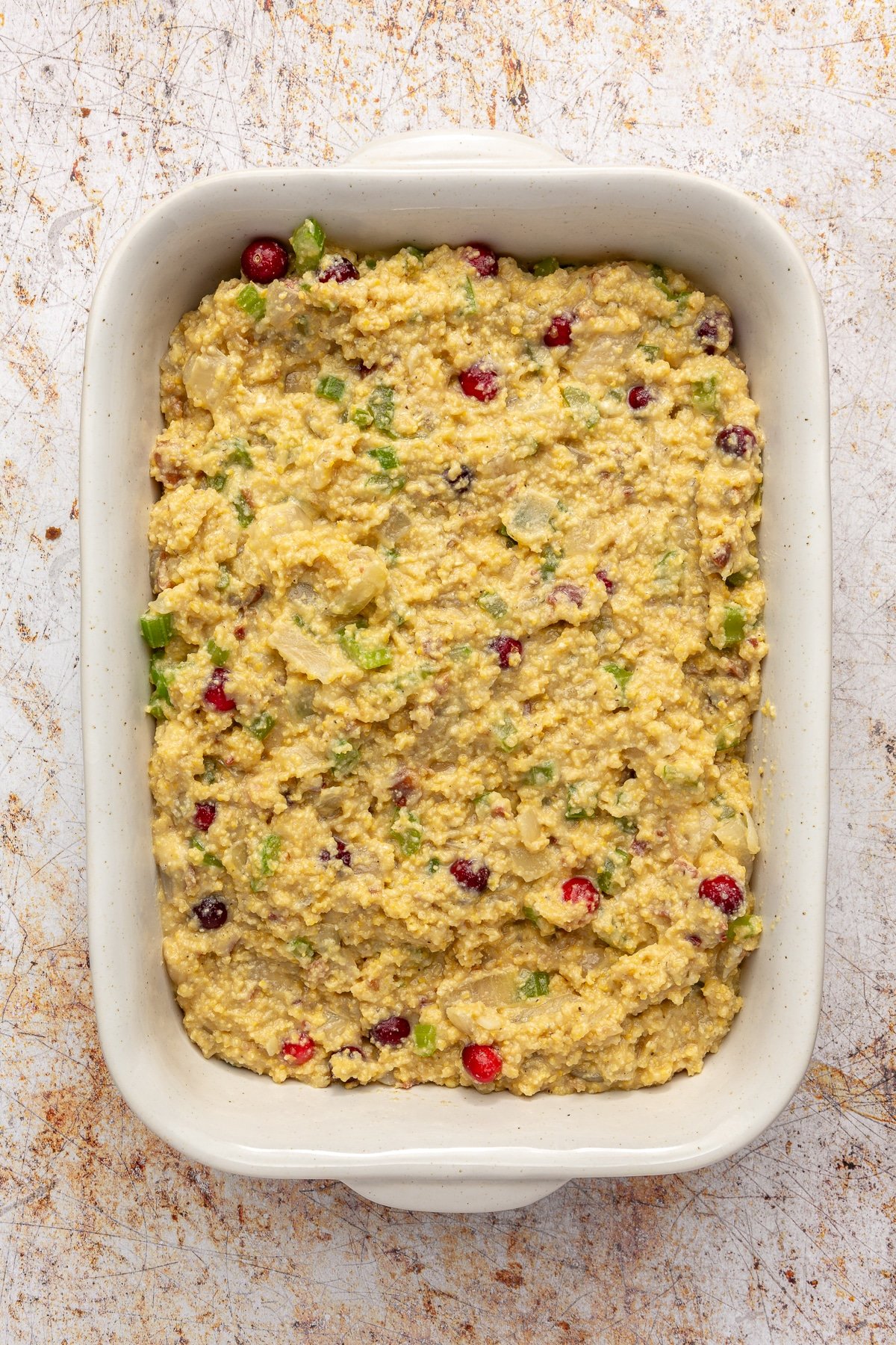 The cornbread, cranberry mixture has been spread evenly in a white, rectangular, baking dish.