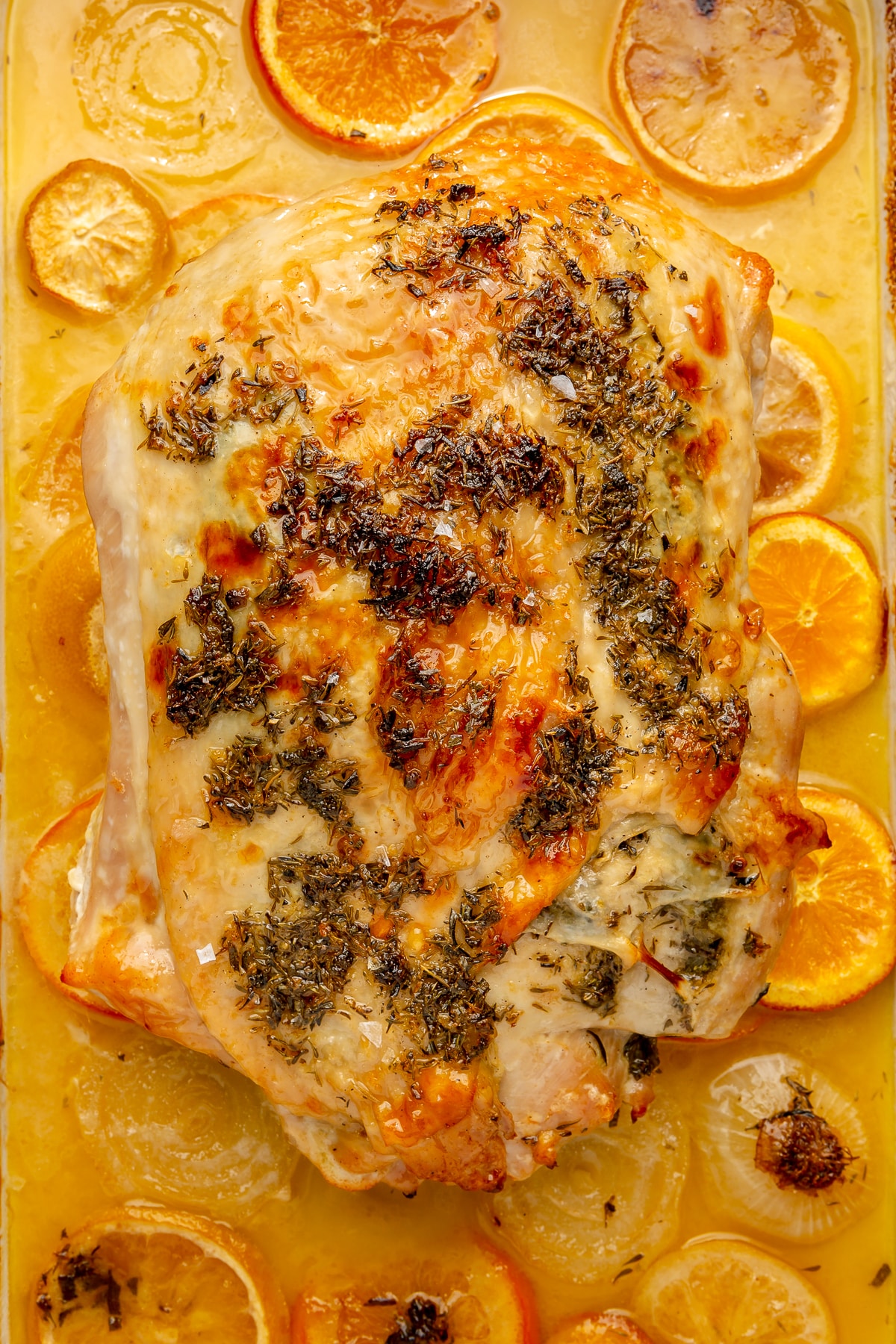 Fully cooked turkey breast is shown surrounded by the, now browned, slices of orange, lemon, and onion.