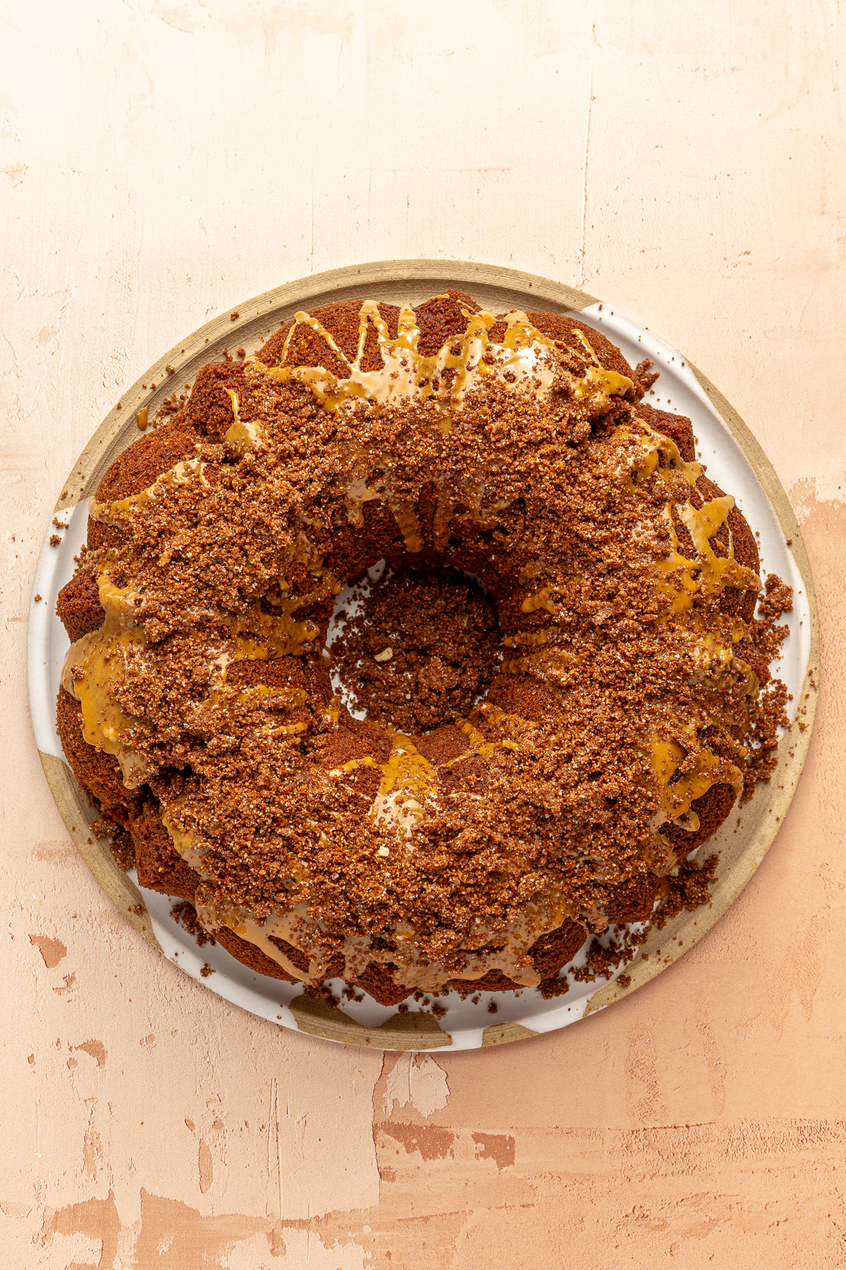 A pumpkin spice bundt cake topped with cold brew icing and a pumpkin spice crumble on a large plate.