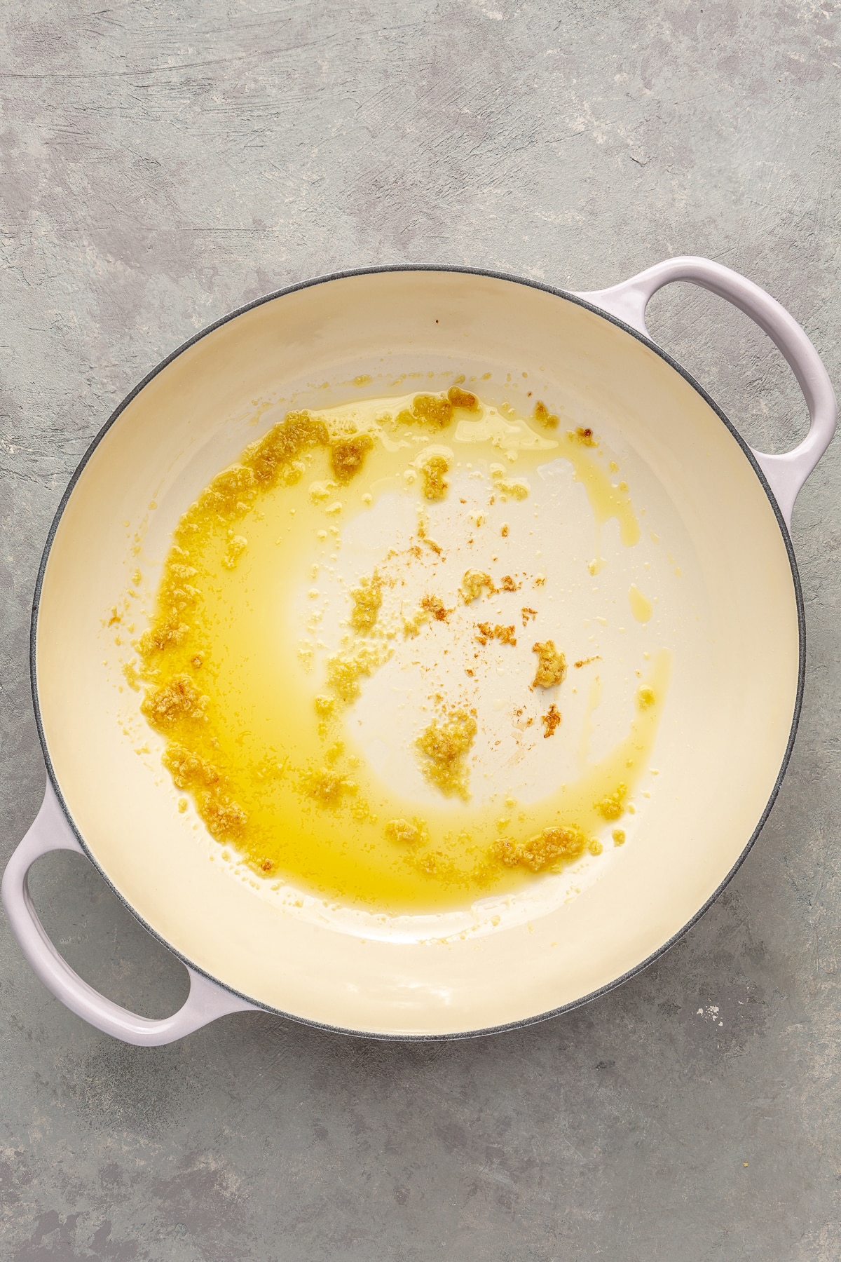 Ghee and minced garlic have been added to a white enameled pot. The ghee has been melted and the minced garlic lightly toasted to a golden brown.
