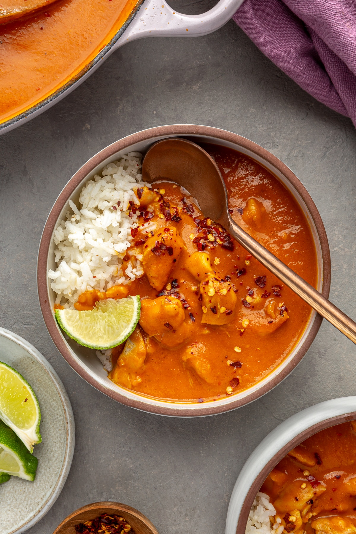 A serving bowl, with rice, has been topped with pumpkin curry. A copper spoon sits inside the bowl along with a slice of lime.