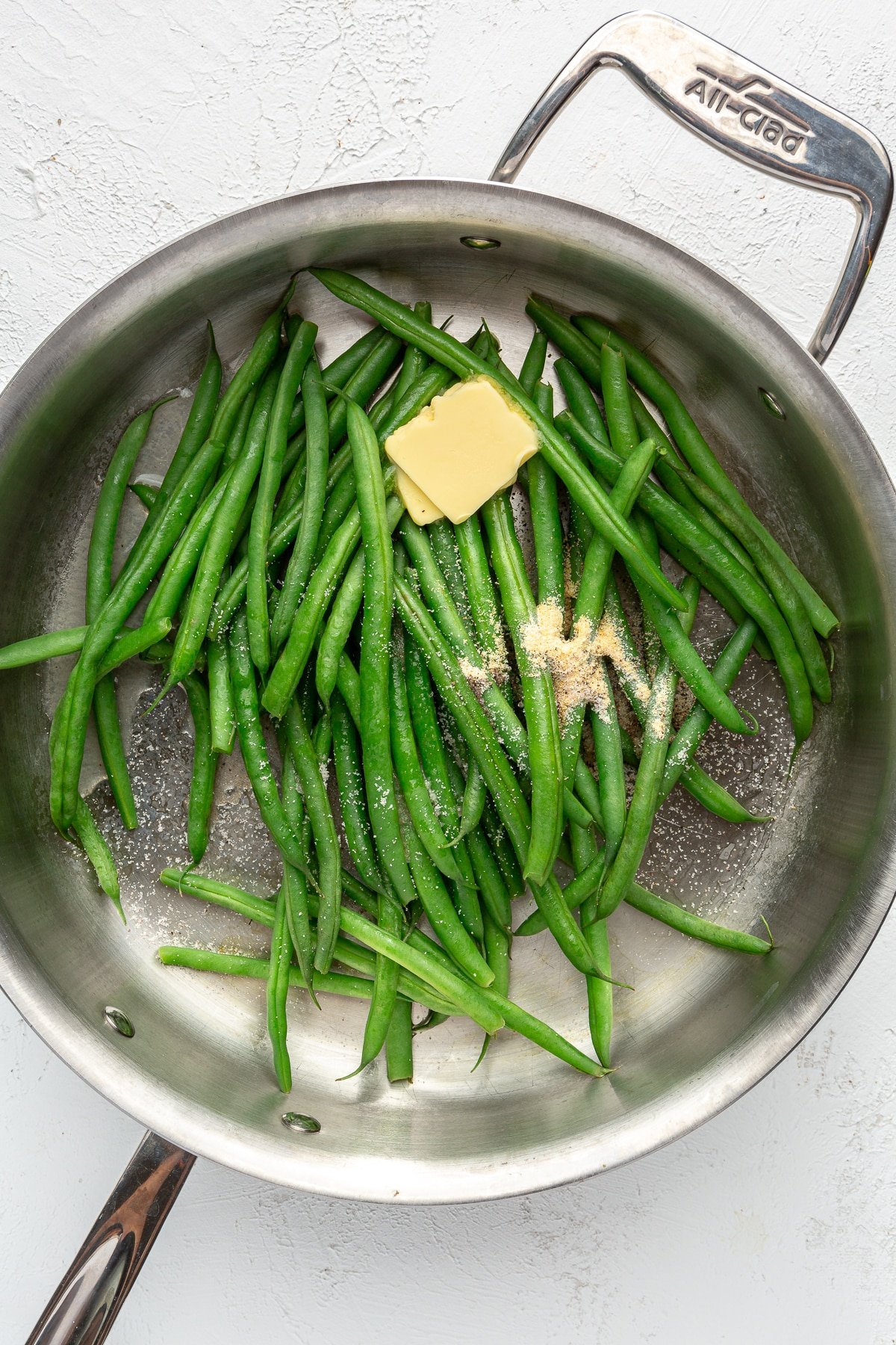A variety of seasoning and butter have been added on top of the green beans.