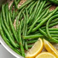 Green beans have been sautéed until soft and slightly browned. Three slices of lemon have been added to the pan.