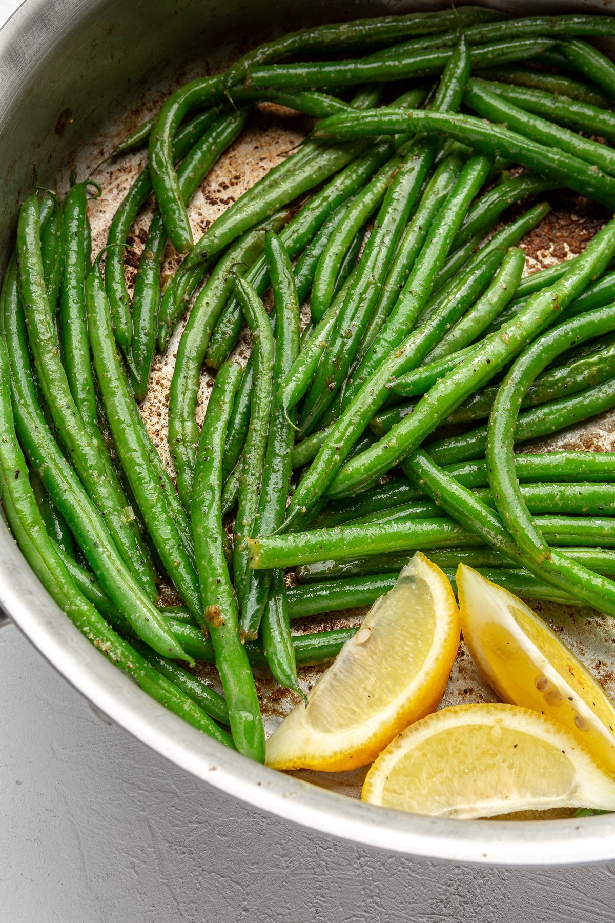 Green beans have been sautéed until soft and slightly browned. Three slices of lemon have been added to the pan.