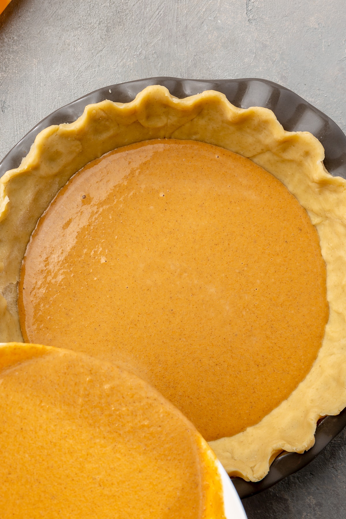 The light orange pumpkin mixture is shown being poured over the raw pie crust in the metal pie dish.