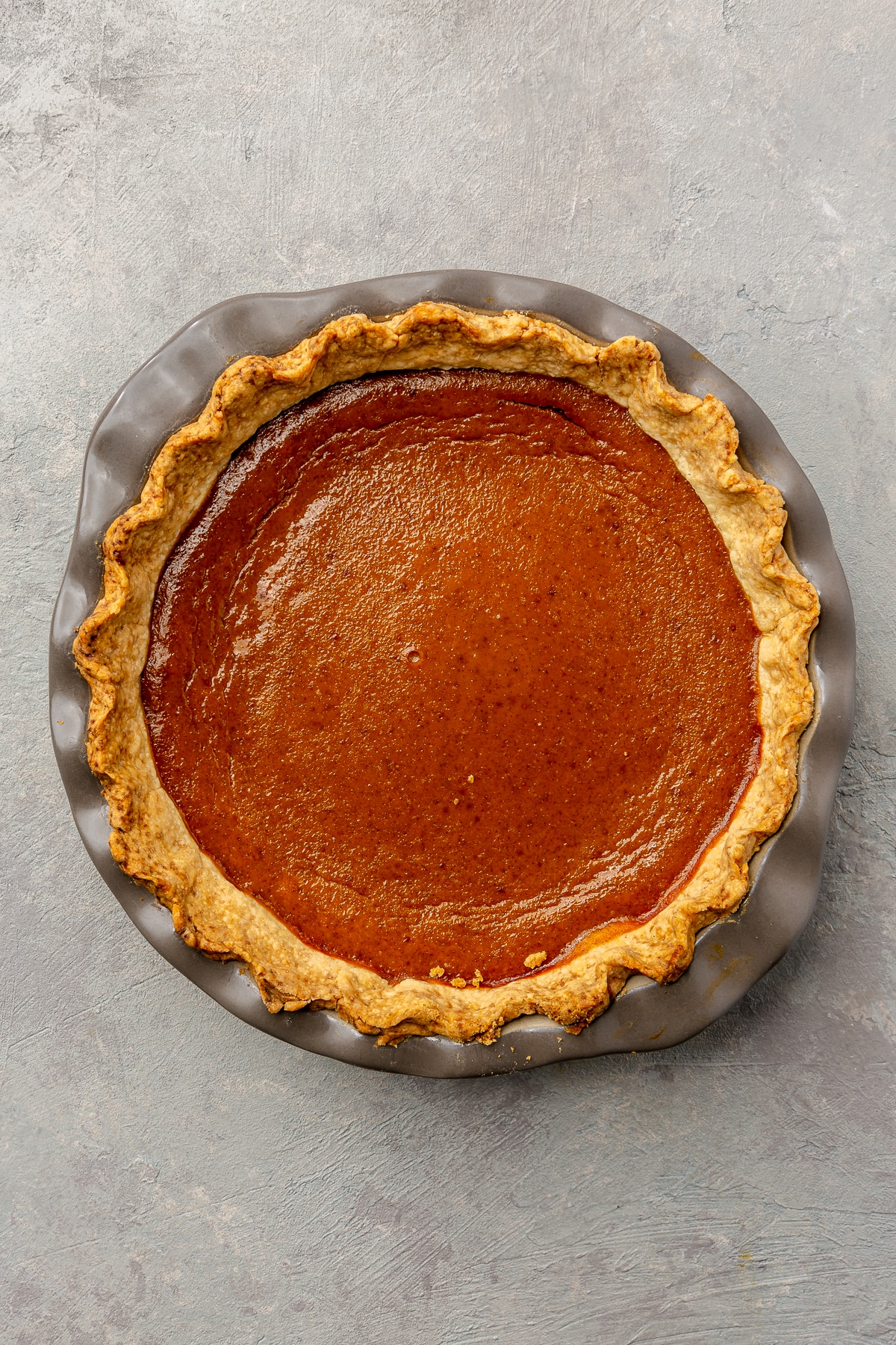 Fully baked pumpkin pie sits in its pie dish on a light grey background.