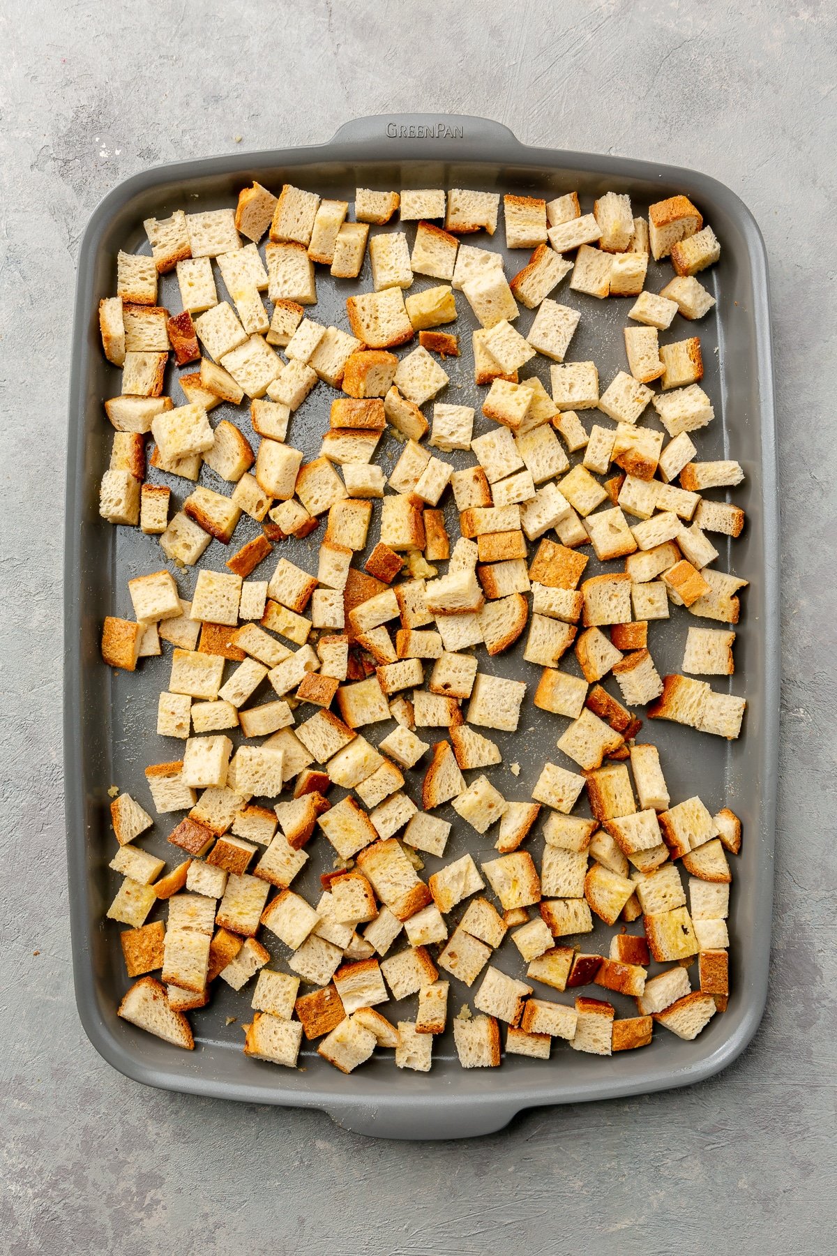 Toasted, lightly golden, pieces of cubed bread sit on a metal baking tray.