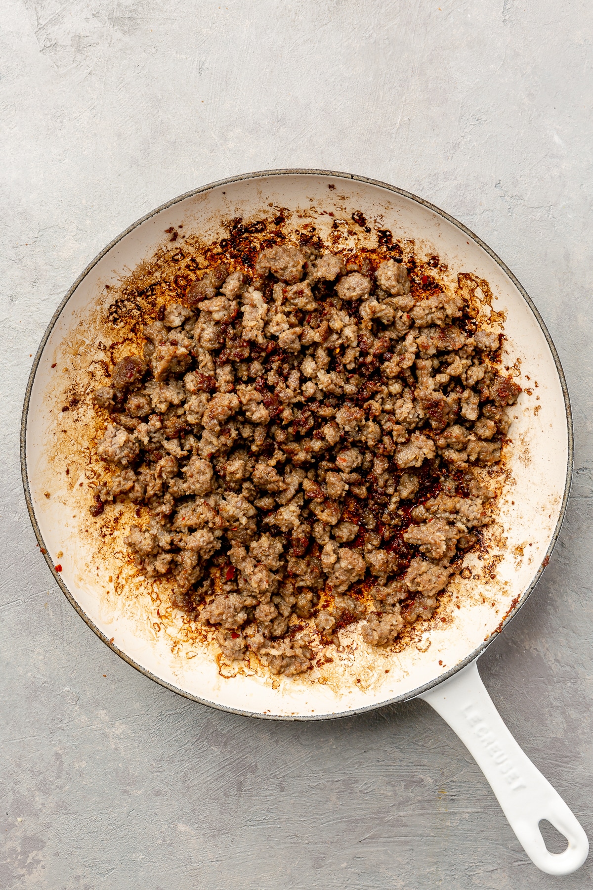 Cooked, browned, ground beef sits in a white frying pan.