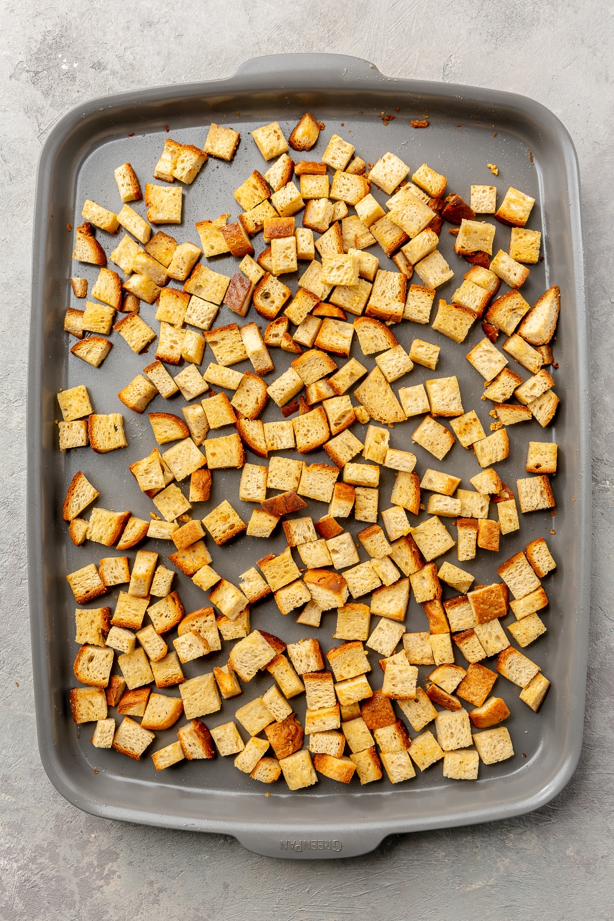 Toasted, lightly golden, pieces of cubed bread sit on a metal baking tray.