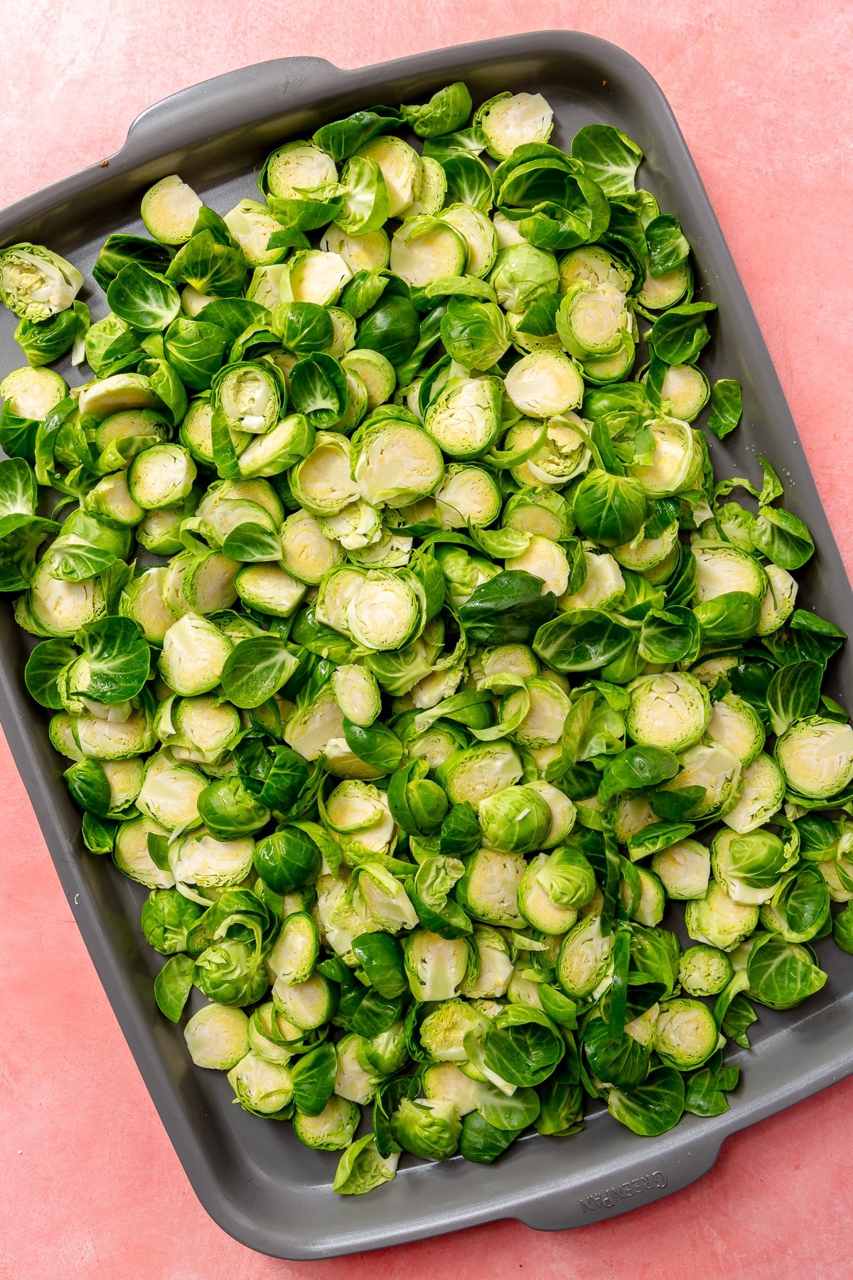 Halved brussels sprouts lay, in an even layer, on a grey baking tray.