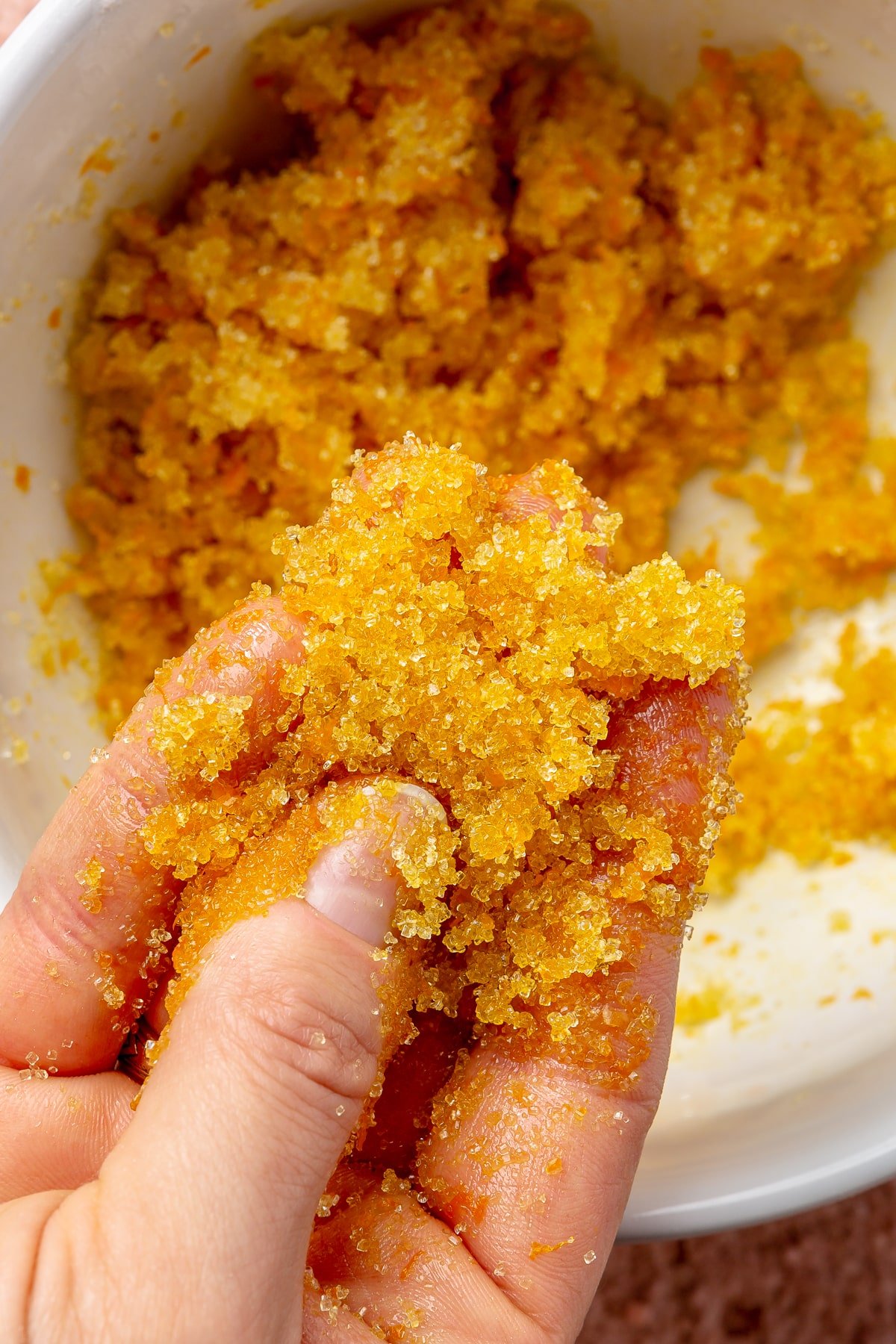 A hand is shown scooping ups bit of an orange sugar mixture.