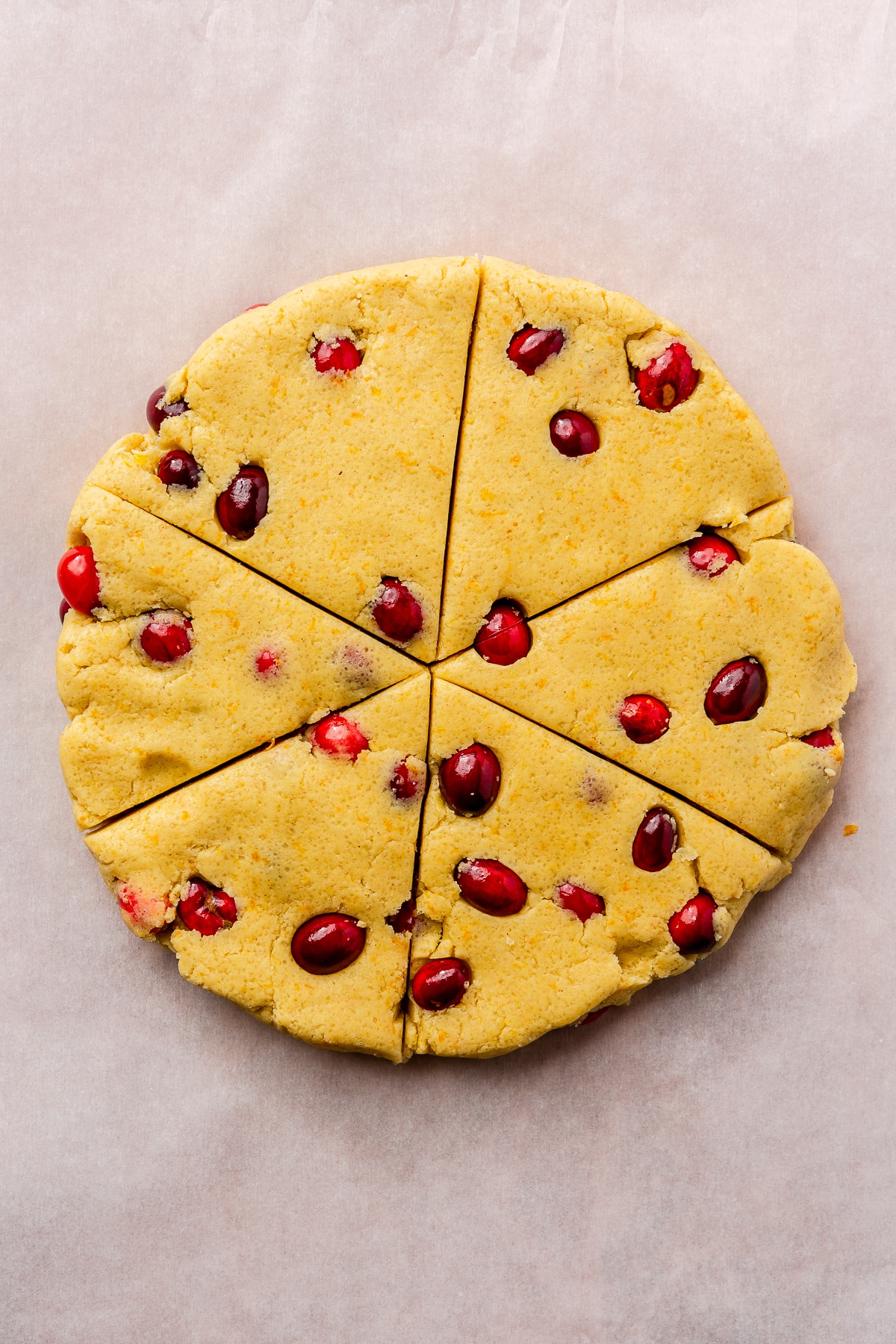 The cranberry, dough mixture has been flattened and formed into a circle shape which has been sliced into six pieces, pizza style.