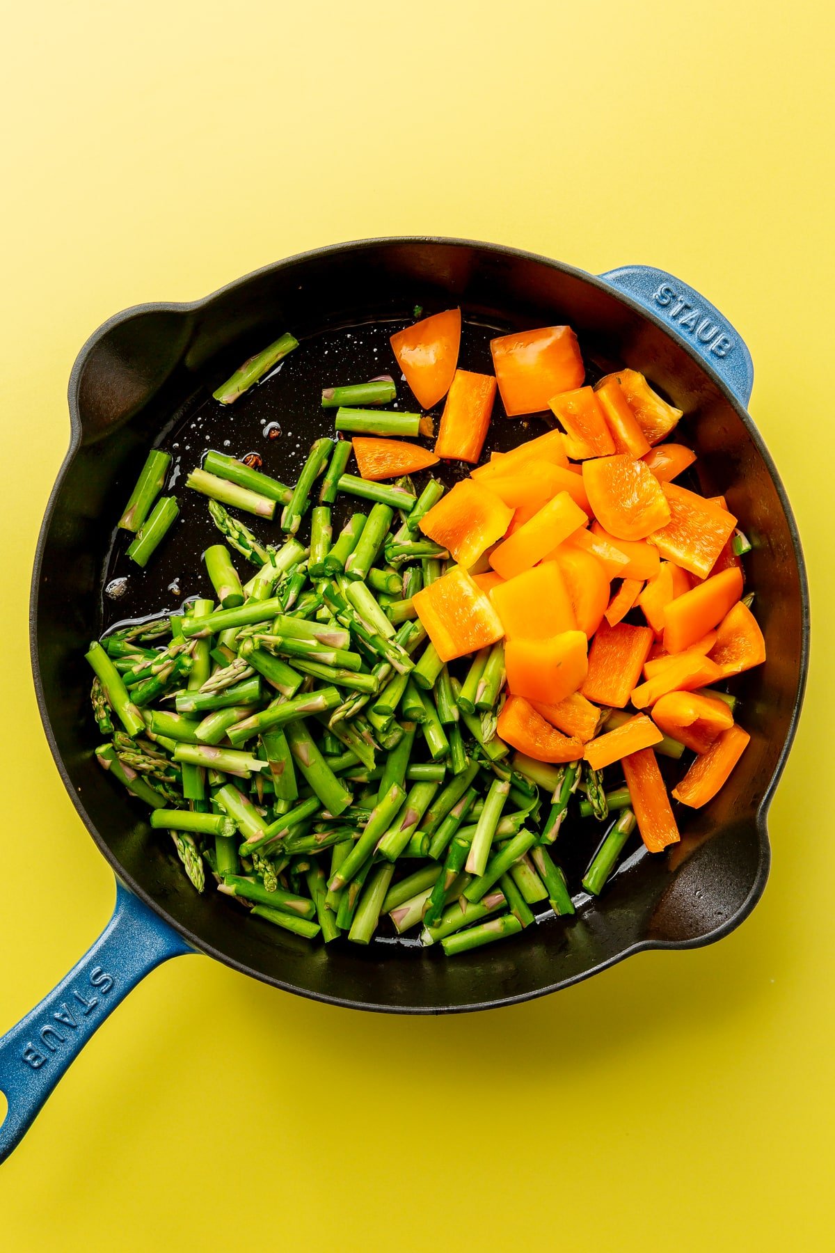 The bacon has been removed from the skillet and been replaced by chopped asparagus and orange bell pepper.