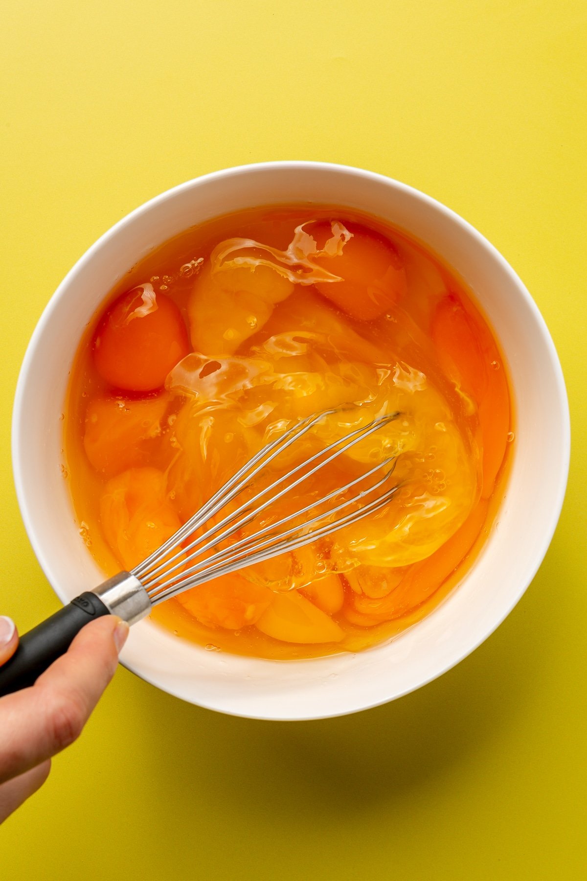 A bowl of eggs are shown being whisked together with a black whisk.
