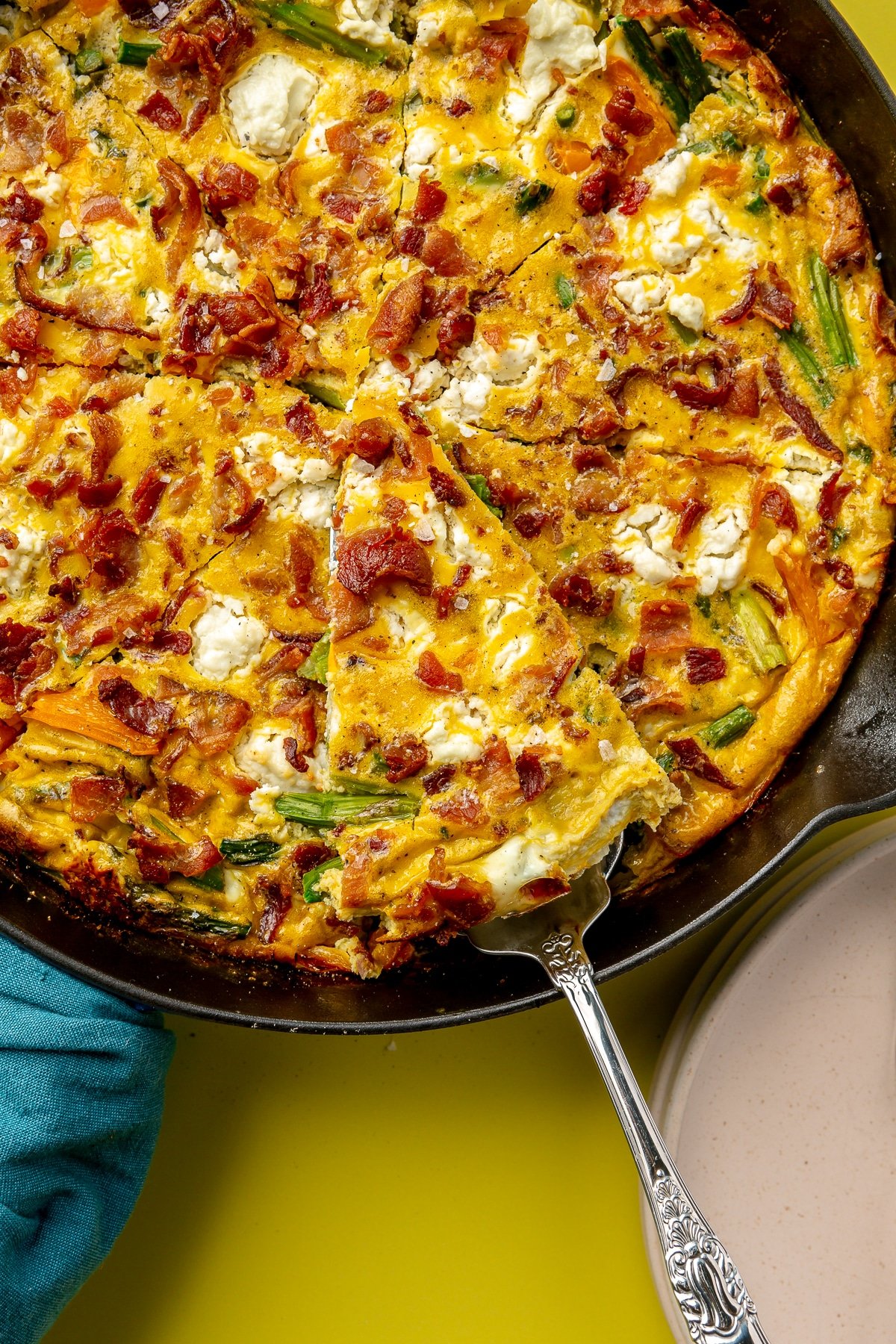 Now fully cooked frittata has been cut into triangular pieces. One piece is shown being removed from the skillet with a silver spatula.