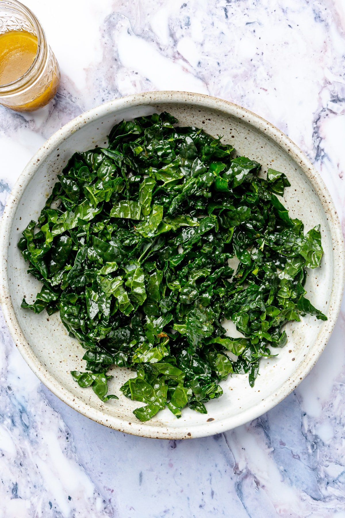 The chopped kale has been placed into a white bowl and covered in the lemon dressing.