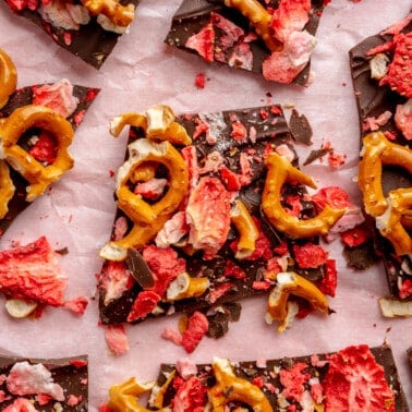 Dark chocolate bark with strawberries and pretzels sits on a light pink paper background.